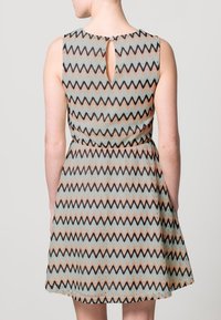 Un vestito senza maniche con un motivo zigzag multicolore in tonalità pastello, dotato di una schiena a occhiello e una vita aderente.