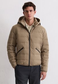 Hellbraune Steppjacke mit Kapuze, vorne mit Reißverschluss, zwei Reißverschlusstaschen und gesteppten Blöcken für Struktur. Schwarze Akzente an den Reißverschlüssen.