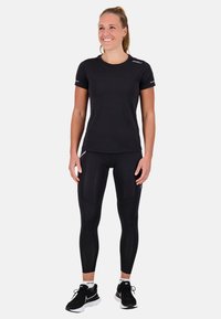 Maglietta sportiva nera a maniche corte e leggings aderenti realizzati in tessuto liscio ed elastico. Indossati con scarpe sportive nere con dettagli bianchi.