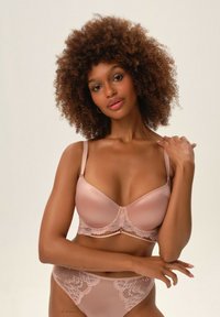 Jasnoróżowy zestaw bielizny składający się z gładkiego satynu i delikatnych koronkowych wykończeń. Biustonosz ma regulowane ramiączka, a majtki mają koronkową nakładkę.