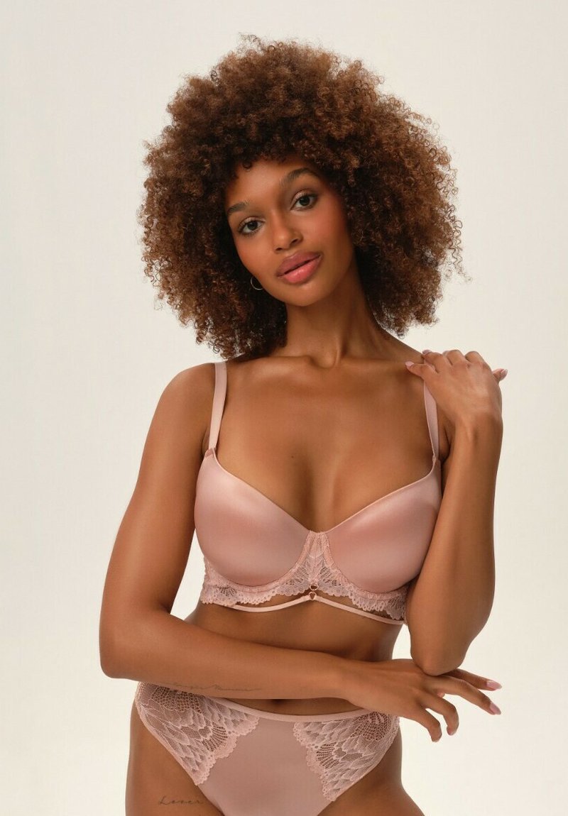 Jasnoróżowy zestaw bielizny składający się z gładkiego satynu i delikatnych koronkowych wykończeń. Biustonosz ma regulowane ramiączka, a majtki mają koronkową nakładkę.