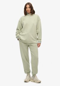 Jasnozielona bluza i dopasowane spodnie dresowe z miękkiego materiału. Bluza ma opuszczane ramiona i małe logo. Stylizacja zestawiona z trampkami.