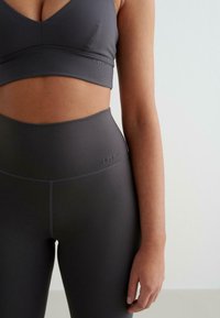 Soutien-gorge de sport gris avec un design en V et des détails de logo, associé à des leggings gris taille haute, fabriqués dans un matériau lisse et extensible.
