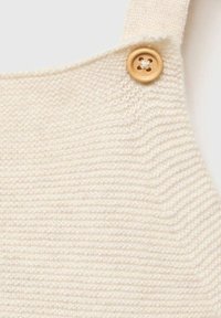 Il tessuto a maglia crema presenta una texture a coste con un dettaglio di pulsante in legno. Il design include spalline regolabili per una vestibilità ottimale.