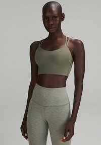 Sostén deportivo verde oliva con tirantes finos y una textura suave, combinado con leggings de cintura alta en gris claro que presentan un sutil patrón jaspeado.