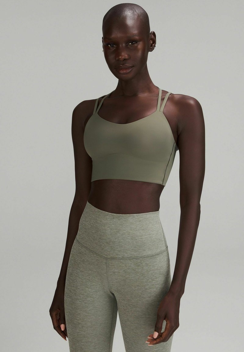 Sostén deportivo verde oliva con tirantes finos y una textura suave, combinado con leggings de cintura alta en gris claro que presentan un sutil patrón jaspeado.