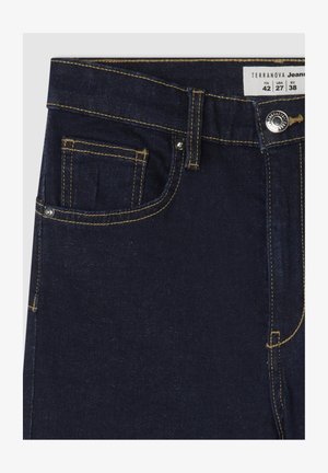 Ciemnoniebieskie dżinsy z żółtym przeszyciem, z standardowymi kieszeniami, metalowym zapięciem oraz metką materiałową na pasku.