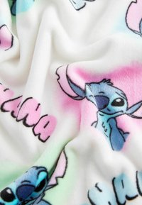 Téli takaró fehér háttérrel, színes, mesebeli Stitch mintákkal és vidám, rózsaszín és zöld árnyalatú felirattal.