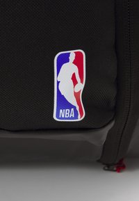 Schwarzer Rucksack mit einem weißen NBA-Logo-Patch und roten sowie blauen Akzenten, aus strapazierfähigem Stoff mit einer strukturierten Oberfläche gefertigt.