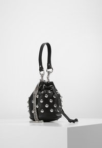 Borsa a secchiello nera con borchie argento e tracolla a catena, esposta su un piedistallo bianco su uno sfondo semplice.