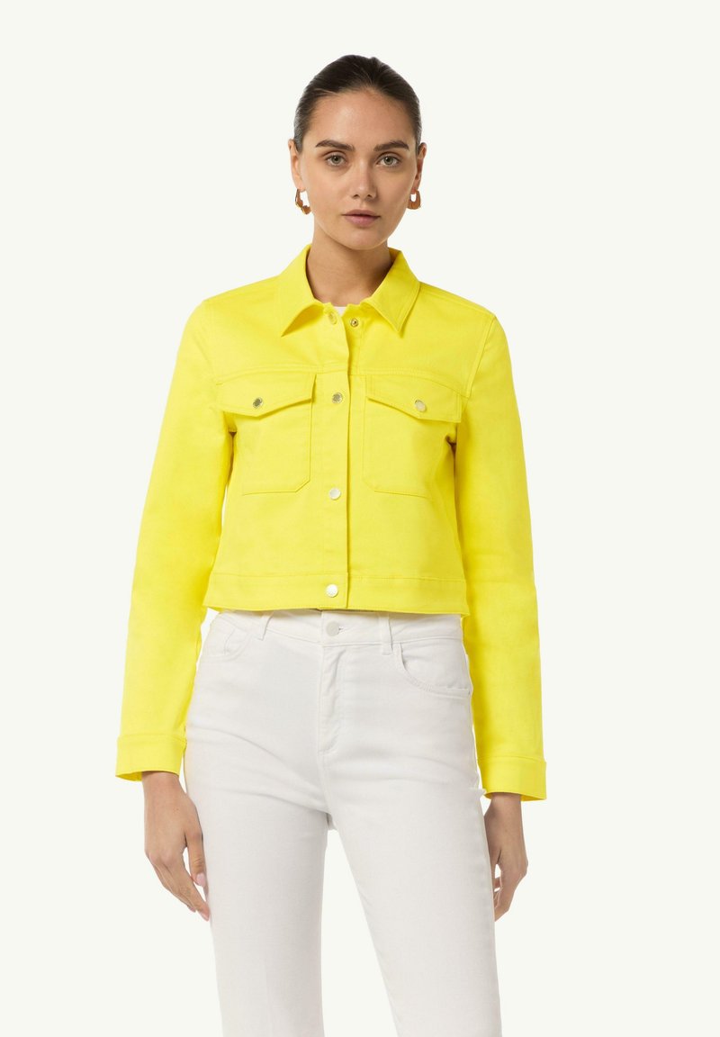 Yellow cropped denim jacket with a button-up front, two chest pockets, and a classic collar; paired with white jeans.