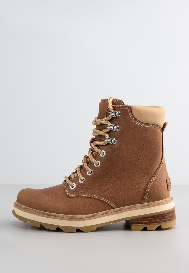 Brauner Leder-Wanderstiefel mit Schnürung, gepolstertem Kragen, metallischen Ösen und dickem, profiliertem Sohlen auf einer hellen Oberfläche.