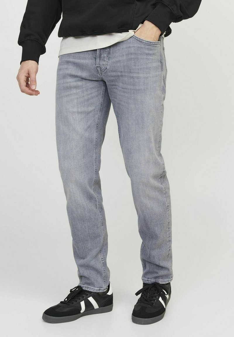 Jeans in denim grigio chiaro con vestibilità dritta, texture sottile, design a cinque tasche e aspetto usurato, abbinati a sneakers nere con dettagli bianchi.