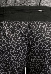 Pantalones cortos de tela negra con un patrón geométrico gris, cintura elástica y un pequeño bolsillo con cremallera en la parte trasera.