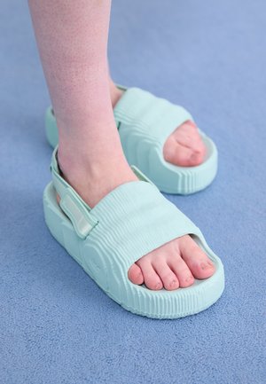 Pieds portant des sandales à plateforme bleu clair se tenant sur une surface texturée bleue.