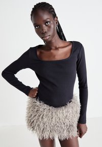 Zwarte top met lange mouwen en een vierkante halslijn, gecombineerd met een lichtgrijze, pluizige, gestructureerde rok. De outfit contrasteert gladde en harige materialen.