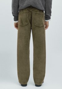 Brune fløjl brede ben bukser har to baglommer og er sat sammen med en grå striktrøje. Stoffet har ribbet tekstur og en let glans.