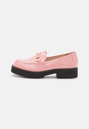 Mocassin rose brillant avec détail de boucle dorée, semelle épaisse noire à crampons, et petit talon bloc, présenté de profil sur fond uni.
