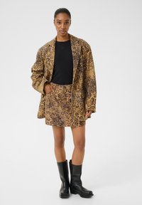 Brauner Leopardenprint-Blazer und Minirock kombiniert mit einem schwarzen Top und knielangen schwarzen Stiefeln. Glatte Textur, oversized Design und auffällige Muster.