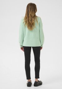 Pull en maille vert menthe avec une coupe décontractée et des épaules tombantes, associé à un jean skinny noir et des chaussures noires épaisses.