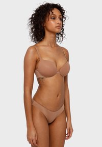 Nackter BH und String-Set aus glattem Stoff. Der BH verfügt über dünne, verstellbare Träger und geformte Cups; der Slip hat ein tief sitzendes Design.