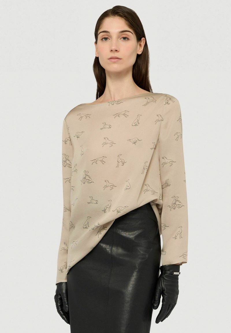 Beige top met lange mouwen en hondenpatroon in zwarte lijnen, gecombineerd met een zwarte leren rok en zwarte handschoenen. Gladde textuur, losse pasvorm.