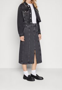 Svart denimjacka med kort design och två framfickor, kombinerad med en matchande lång svart denimkjol som har en slits fram och sömnadsdetaljer.