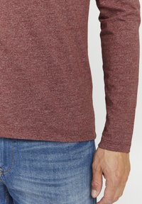 Langermet bordeaux skjorte med teksturert finish, sammen med blå denim jeans. Skjorten har rund hals og tettsittende ermer.