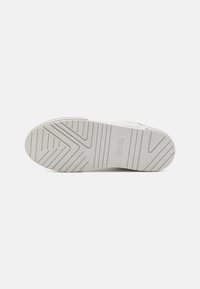 Suela de zapatilla blanca con una superficie de goma texturizada, que presenta un patrón diagonal y un logotipo. Diseño robusto y plano, adecuado para el uso diario.