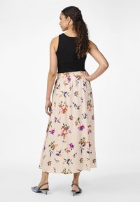 Haut sans manches noir associé à une longue jupe maxi beige à fleurs flottante, ornée de motifs colorés et dotée d'une taille élastique.