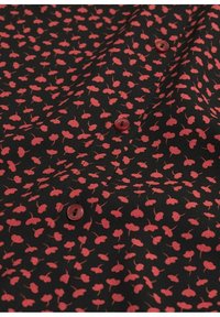 Tissu noir avec un petit motif floral rouge, agrémenté de boutons rouges. La texture semble lisse, mettant en valeur le design délicat.
