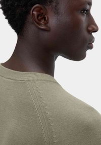 Maglione lavorato a maglia in verde oliva, con collo rotondo, cuciture testurizzate lungo le spalle e una finitura liscia sul corpo.