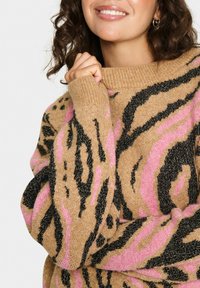Maglione beige con stampa leopardata nera e rosa, caratterizzato da un collo ampio e un tessuto lavorato. Il tessuto ha una leggera lucentezza.