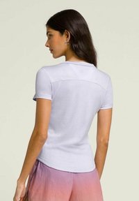 Camiseta de manga corta en un suave color púrpura claro, con un cuello redondo y un logo sutil en la parte superior de la espalda. Textura suave, diseño ajustado.