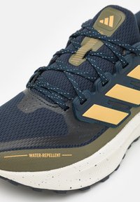 Navy athletic shoe with mesh upper, water-repellent features, dark green accents, and yellow branding. Textured rubber sole with detailed tread.