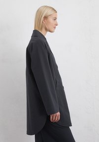 Palton lung de culoare gri închis, cu guler, buzunare laterale și margine curbată. Fabricat dintr-un material neted, cu un croi lejer și un design minimalist.