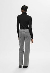Zwarte geribbelde coltrui gecombineerd met hoog-waist grijze jeans. De outfit heeft lange mouwen en een ontspannen rechte pasvorm.