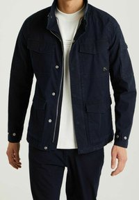 Navy blue jacket featuring a zip closure, multiple front pockets, button cuffs, and a textured, durable fabric.