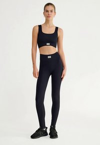 Top deportivo corto negro acanalado y leggings de cintura alta, ambos con detalles de la marca, combinados con zapatillas deportivas negras.