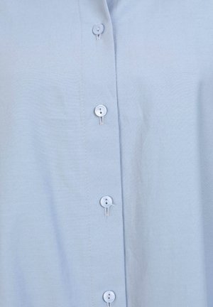Una camicia leggera azzurro chiaro realizzata in tessuto morbido, con colletto alla coreana e sei piccoli bottoni rotondi azzurri lungo la parte anteriore.