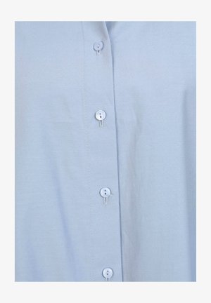 Světle modrá košile na knoflíky vyrobená z hladkého materiálu, má stojáčkový límec a šest malých, kulatých, světle modrých knoflíků vpředu.