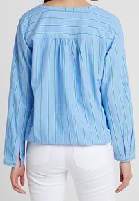 Blouse longue à manches longues bleu clair avec des rayures verticales vertes, un dos froncé et des poignets boutonnés. Fabriquée dans un tissu doux et texturé.