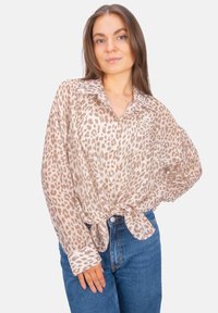 Lightweight, sheer button-up shirt in beige with brown leopard print, featuring a collar and knotted front. Paired with blue jeans.