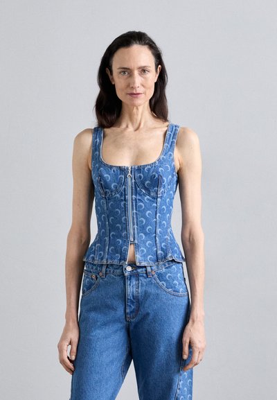 Corset en denim avec un motif bleu, décolleté carré, fermeture éclair et design ajusté ; associé à un jean bleu assorti avec un léger dégradé.