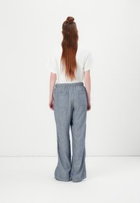 Lyseblå, strukturerede brede bukser med elastisk talje og to baglommer. Båret med en plain hvid t-shirt med korte ærmer.