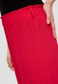 Rode geplisseerde broek van een textuur, lichtgewicht materiaal. Bevat een geraffineerde tailleband en een zijzak, weergegeven gestyled op de heup.