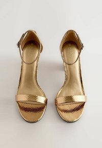 Arany fémből készült szandál, amelynek textúrázott kígyóbőr mintázata van, nyitott orrú kialakítással, bokapánttal és alacsony wedge sarkú. Simább belső bélés.