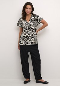 Black and cream zebra print top with short sleeves, V-neck design, paired with loose-fitting black trousers and black flat shoes.