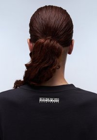 Schwarzes Baumwoll-T-Shirt mit Rundhalsausschnitt, das auf der Rückseite ein weißes Markenlabel zeigt. Der Stoff wirkt glatt und körpernah.
