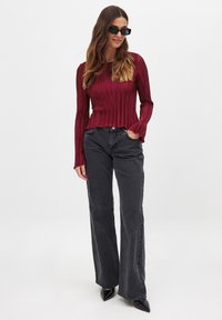 Burgundy plissert langærmet top parret med mørke flared jeans og sorte spidse hæle. Toppen har en bølget kant og struktureret stof.
